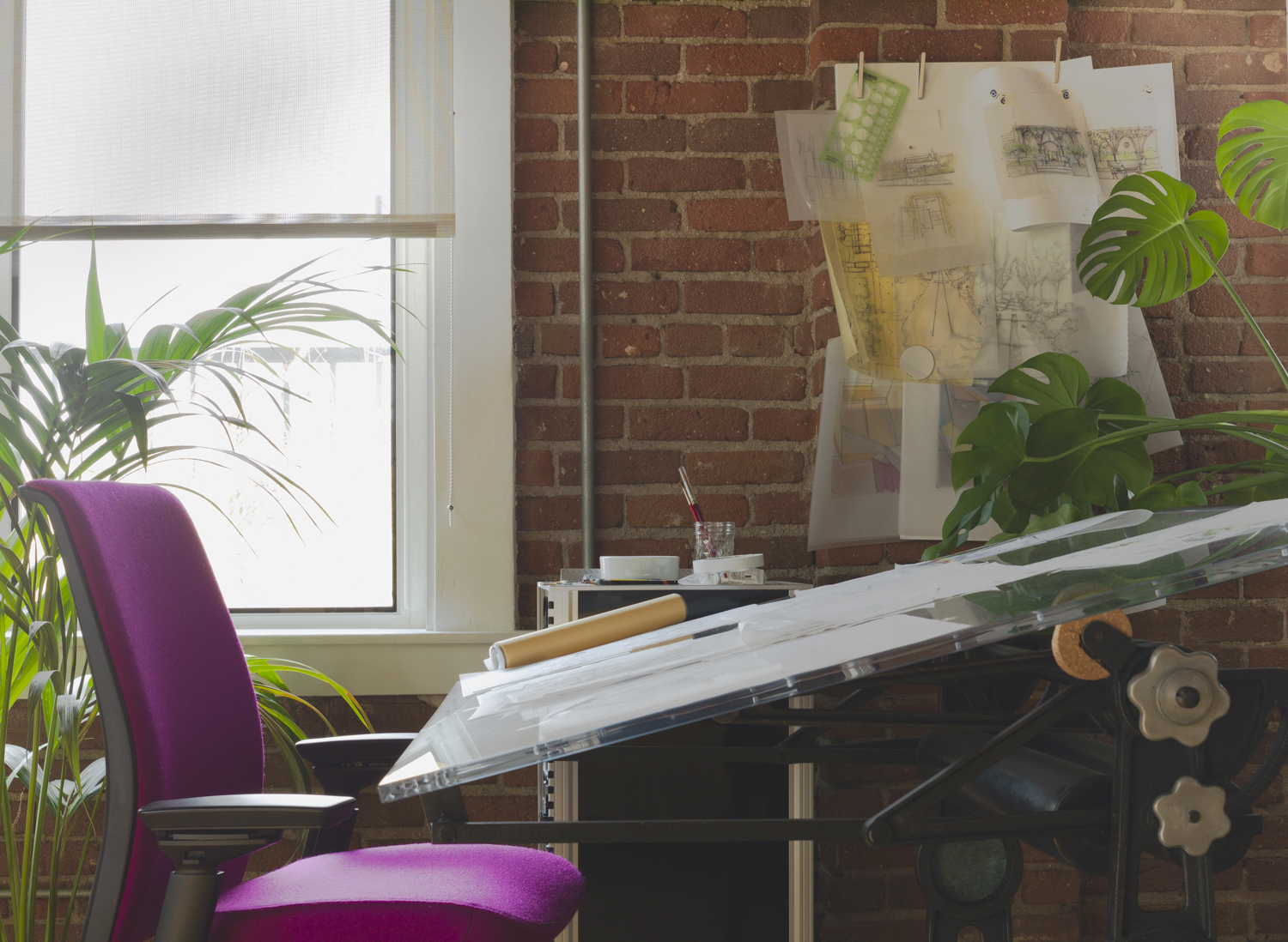 An interior view of the WVH Design studio; a purple architect's chair at a drafting table covered in drawings and surrounded by tropical plants.